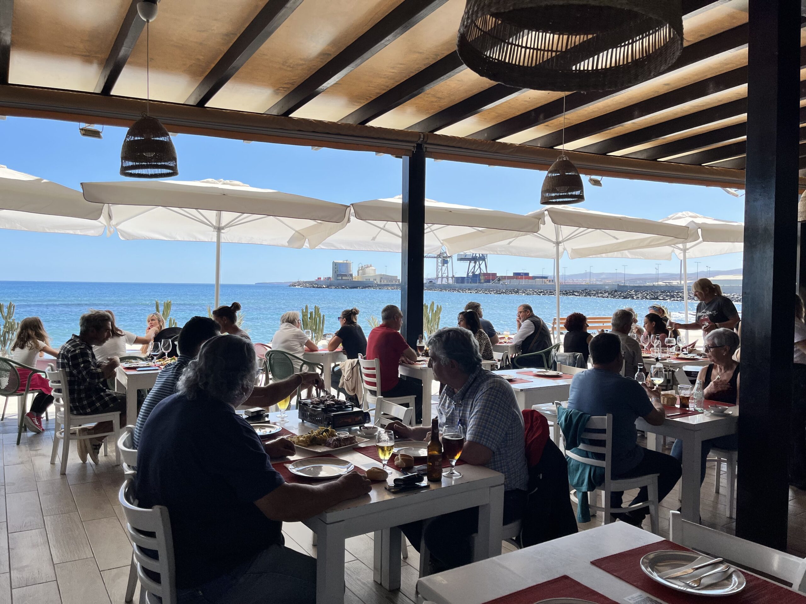Clientes disfrutando en el comedor con la terraza abierta y el mar de fondo