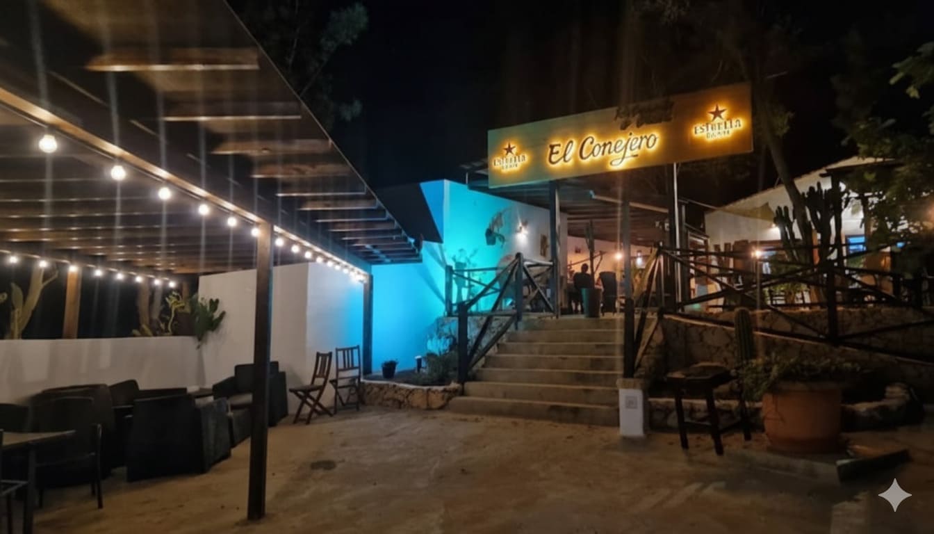 Terraza exterior del Restaurante El Conejero por la noche, iluminada con guirnaldas de luces cálidas y una luz azul ambiental, creando una atmósfera acogedora.