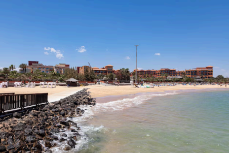Paseo marítimo de piedra y madera junto a la playa de la Guirra con complejos hoteleros al fondo.