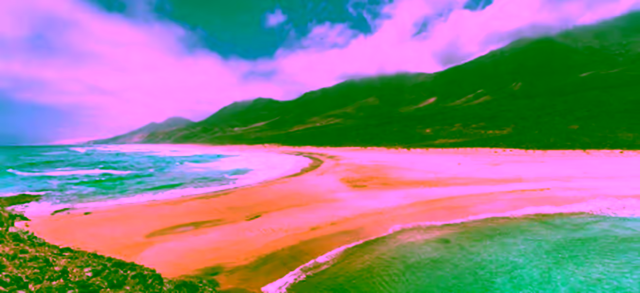 Vista panorámica de la Playa de Cofete con su arena dorada, el mar turquesa y las montañas de fondo bajo un cielo con nubes.