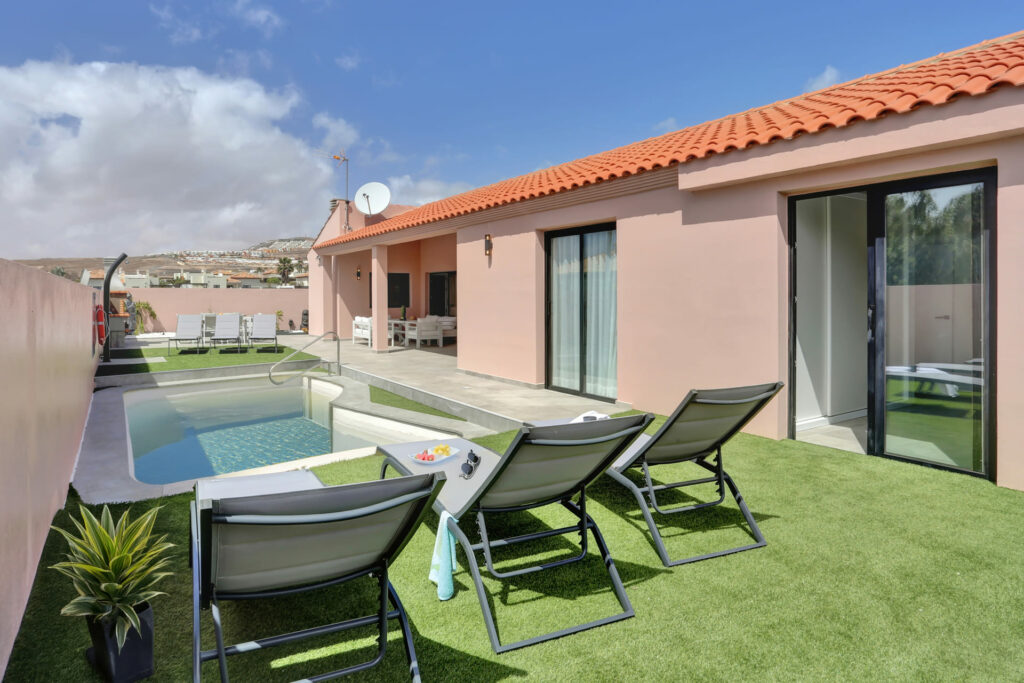 Piscina junto a jardín artificial con hamacas y fachada en tonos rosados