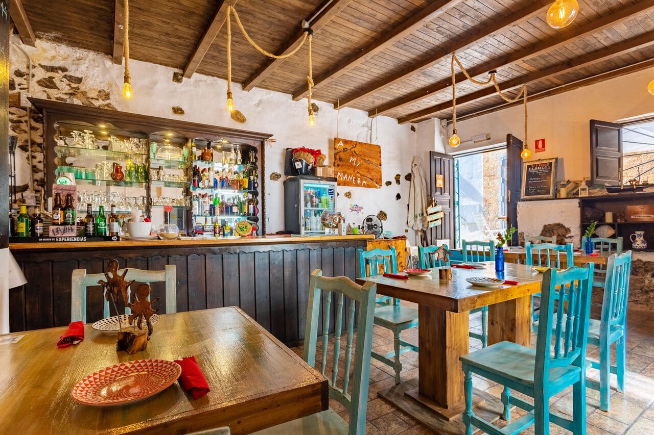 Primer plano de mesa con vajilla y al fondo la barra con copas y botellas en A Mi Manera.