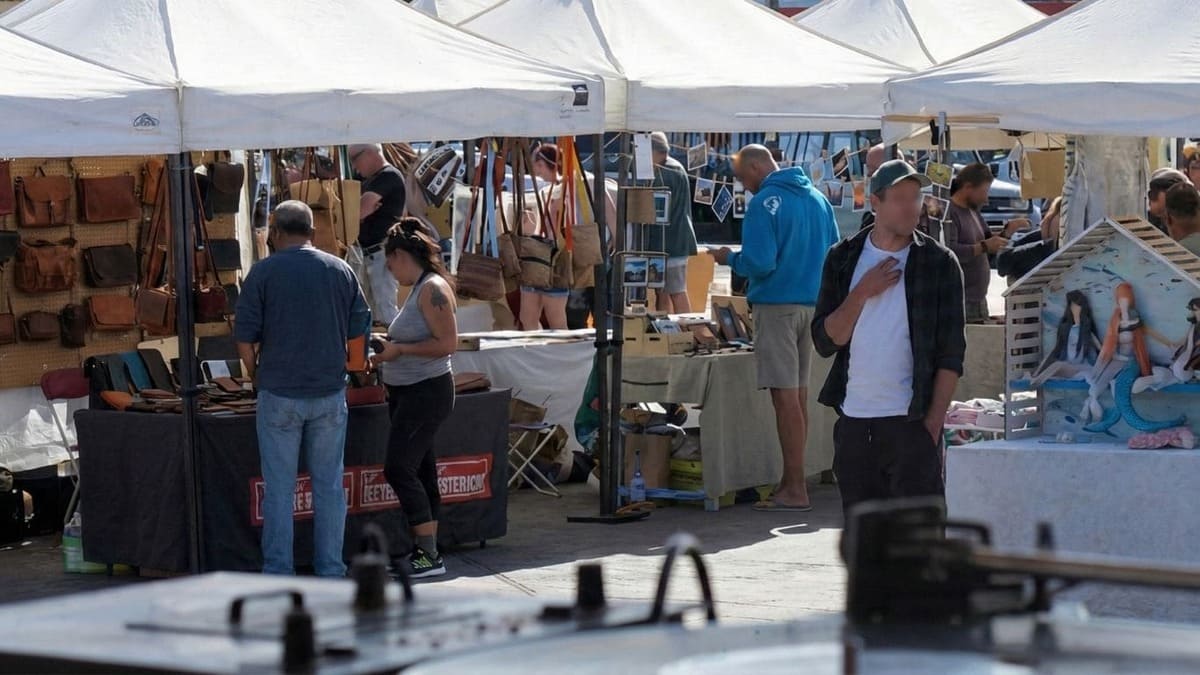 Puestos de artesanía en el Mercadillo de Lajares, con carpas blancas y visitantes comprando productos locales en la plaza.