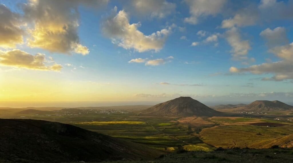 Vista panorámica de Vallebrón al atardecer, con valle verde, montañas y cielo con nubes en Fuerteventura.