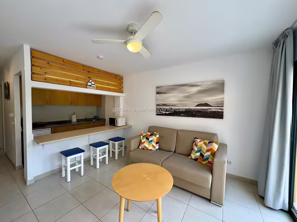 Salón con sofá beige y barra de madera con taburetes en Fuerteventura.