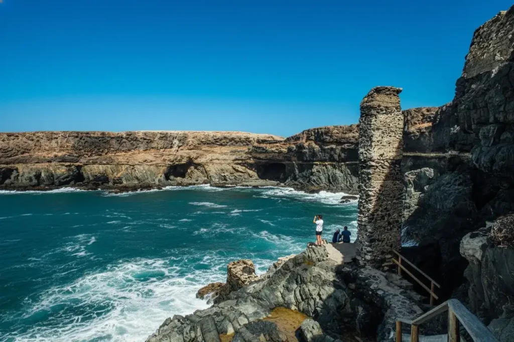 Visitantes en una plataforma de piedra observando acantilados con ruinas históricas y aguas turquesas del océano