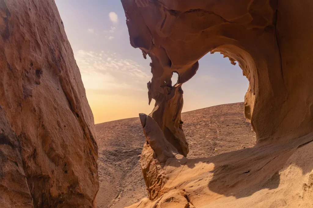 Arco natural de roca roja y marrón en desierto árido con vistas al horizonte durante la puesta de sol