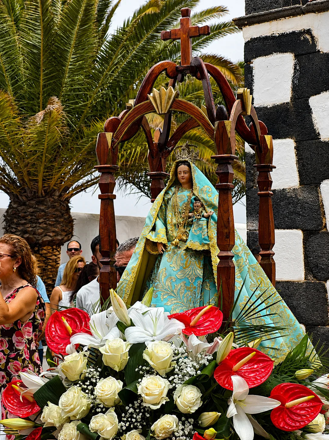 Imagen procesional de la Virgen engalanada con flores rojas y blancas durante las fiestas patronales de un pueblo de Fuerteventura