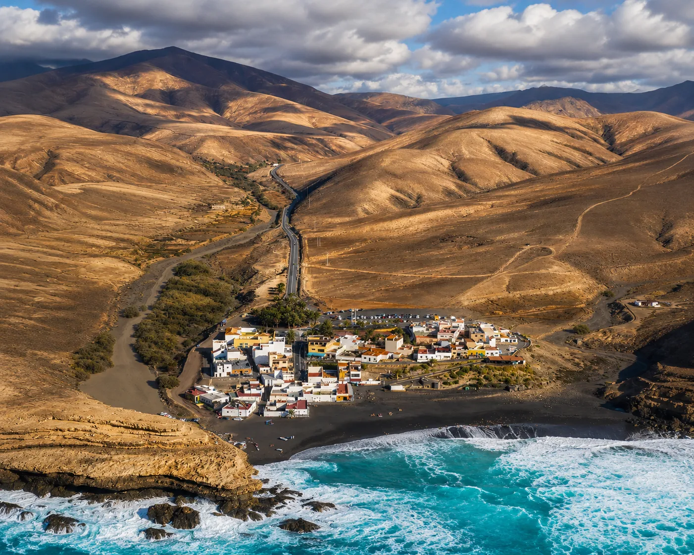 Vista panorámica aérea del pueblo marinero de Ajuy, su playa de arena volcánica negra y el barranco rodeado de formaciones áridas en la costa oeste de Fuerteventura.