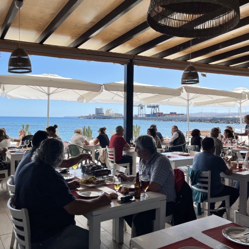 Clientes disfrutando en el comedor con la terraza abierta y el mar de fondo