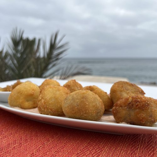 Bandeja de croquetas doradas con vista al mar de fondo