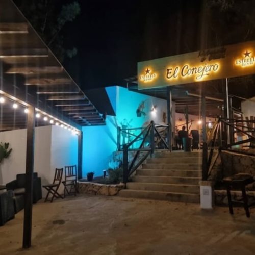 Terraza exterior del Restaurante El Conejero por la noche, iluminada con guirnaldas de luces cálidas y una luz azul ambiental, creando una atmósfera acogedora.