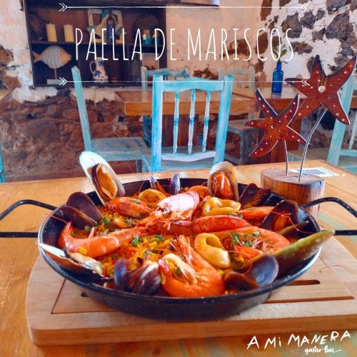 Paella de mariscos con gambas, mejillones y calamares servida en paellera sobre mesa de madera.
