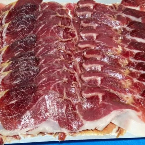 Plato grande con abundantes lonchas de jamón ibérico recién cortado a cuchillo, mostrando el veteado de grasa y el color intenso de la carne.