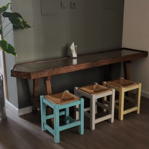 Banco de madera antiguo con taburetes de colores y planta en lechera metálica en La Puipana