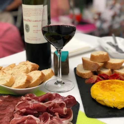 Mesa de un restaurante con un aperitivo de tapas españolas: raciones de jamón serrano y tortilla de patatas, pan, y una copa de vino tinto.