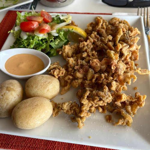 Plato de puntillas de calamar fritas servido con tres papas arrugadas, una pequeña ensalada de lechuga y tomate, y un cuenco con salsa mojo.