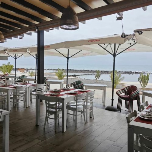 Terraza frente al mar de El Rinconcito de Doña Juanita, mesas preparadas bajo sombrillas con vistas al océano en Fuerteventura.