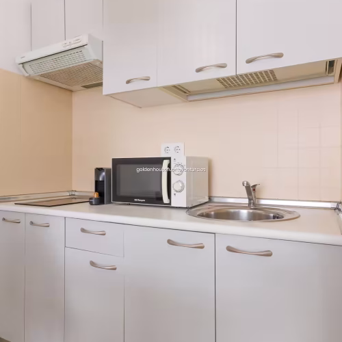 Muebles de cocina blancos con tiradores metálicos, fregadero de acero y extractor