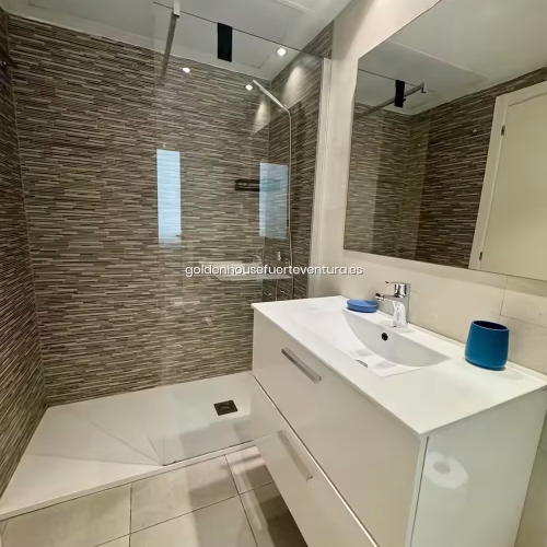 Baño con mampara de cristal, plato de ducha blanco y paredes con azulejos marrones.