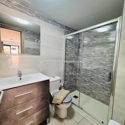 Cuarto de baño con plato de ducha, mampara de cristal y mueble moderno.