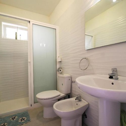 Baño con paredes onduladas blancas, lavabo de pie, bidé y plato de ducha.