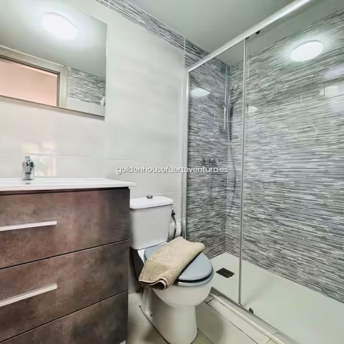 Baño con azulejos grises, mampara de cristal y mueble de lavabo moderno en Fuerteventura