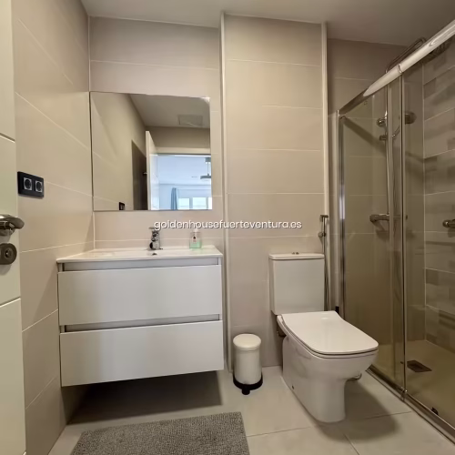 Cuarto de baño con mueble de lavabo suspendido blanco, inodoro y mampara de cristal.