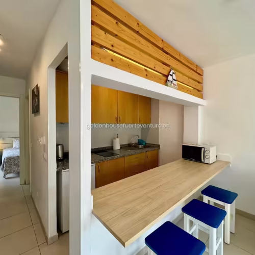 Vista de la barra de madera con taburetes azules y pasillo hacia el dormitorio en Fuerteventura.