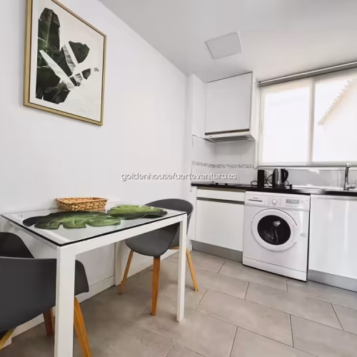 Cocina blanca moderna con mesa de comedor y sillas grises en Corralejo