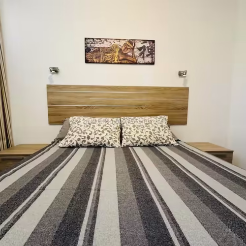 Primer plano del cabecero de madera con mesitas a juego y cuadro de estilo zen.