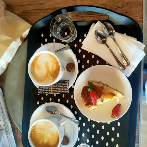 Bandeja servida con dos cafés con leche y una porción de tarta de queso casera decorada con fresas en el restaurante Aroma de Sal.