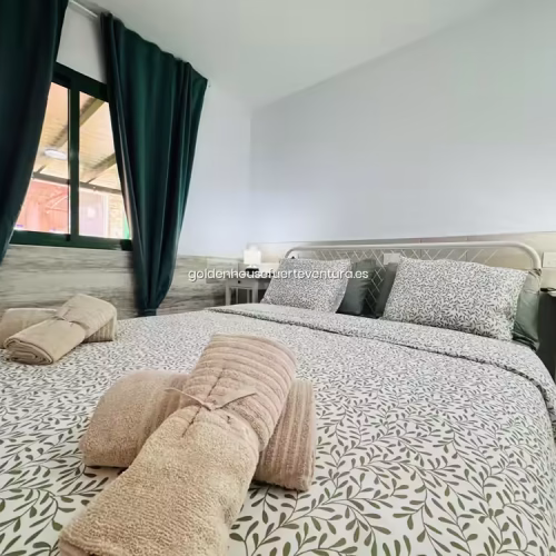 Cama de matrimonio con textiles de motivos vegetales y cortinas opacas en tonos verde oscuro.