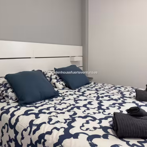 Cama grande con almohadas decorativas azules y juegos de toallas oscuras enrolladas.