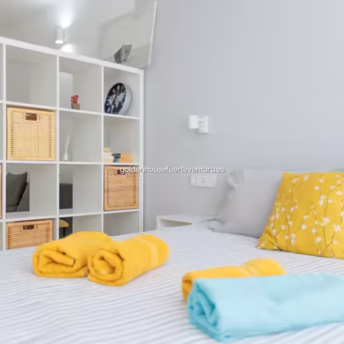 Cama con ropa de rayas y toallas enrolladas en colores amarillo y azul sobre el edredón