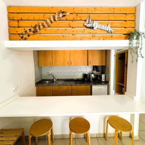 Cocina compacta equipada con microondas, cafetera y barra con taburetes.