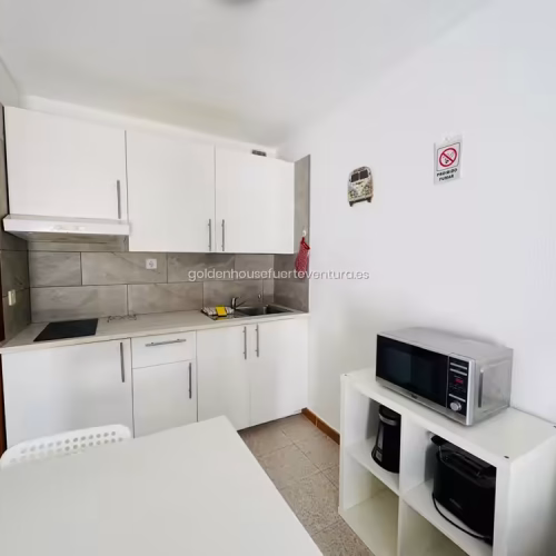 Cocina compacta de muebles blancos con placa, fregadero, microondas y cafetera.