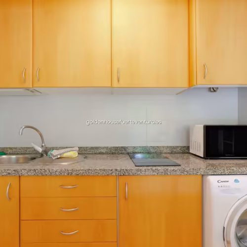 Cocina con muebles de madera, encimera de granito y lavadora blanca.