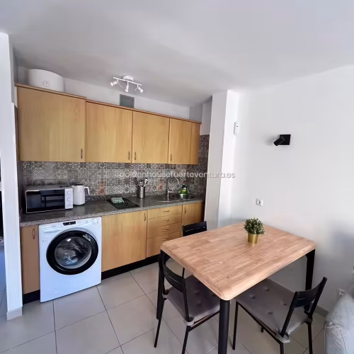 Frente de cocina con armarios de madera, lavadora integrada, microondas y placa.