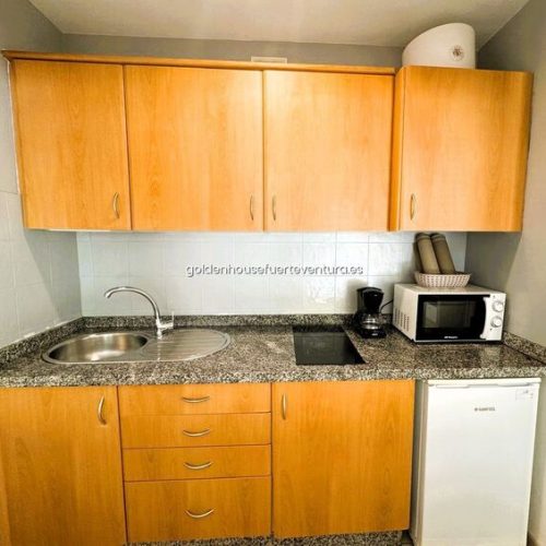 Muebles de cocina de madera con fregadero, vitrocerámica, microondas, cafetera y nevera pequeña.
