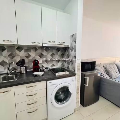 Cocina compacta con lavadora y vitrocerámica junto a zona de estar en Fuerteventura