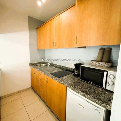 Cocina de madera con encimera de granito, microondas, cafetera y fregadero de acero inoxidable.