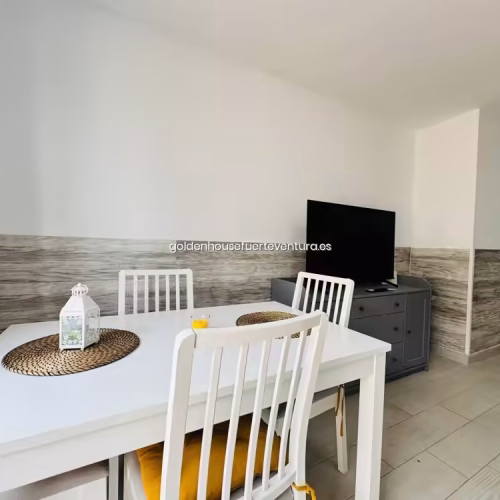 Comedor con una mesa blanca y 4 sillas blancas en un salón con una televisión