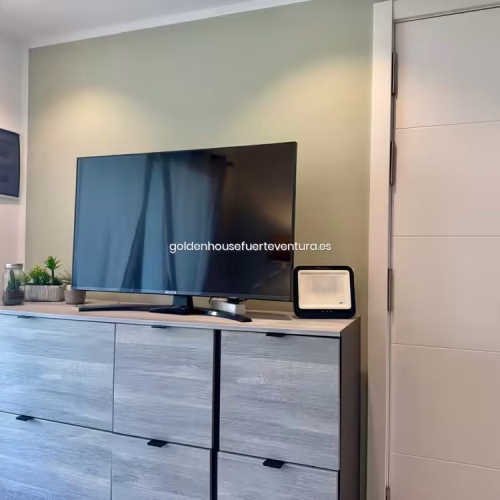 Televisión sobre mueble gris junto a puerta de entrada blanca en apartamento Corralejo Sun 105.