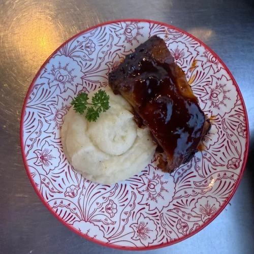 Plato de costillas con salsa barbacoa y guarnición de puré de patatas servido en el restaurante Aroma de Sal.