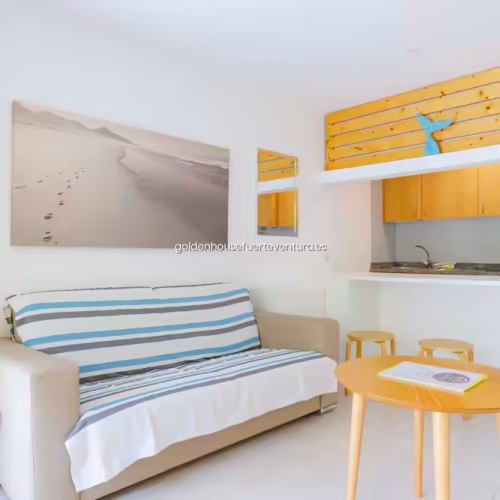 Salón con luz natural, cuadro de dunas y detalles decorativos en la pared.