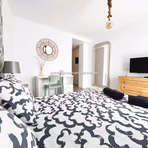 Cama con ropa de cama geométrica frente a cómoda de madera con televisión.
