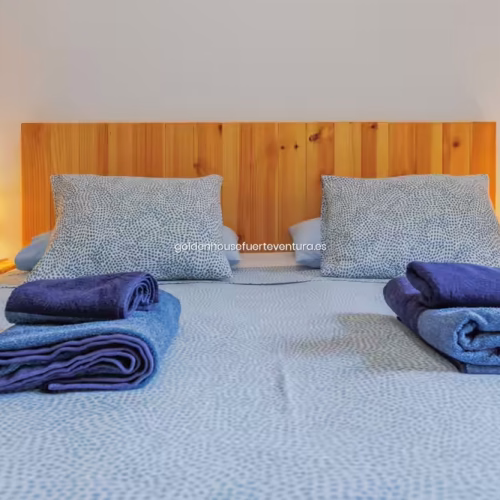 Primer plano de cama de matrimonio con toallas azules dobladas y cabecero de listones de madera.