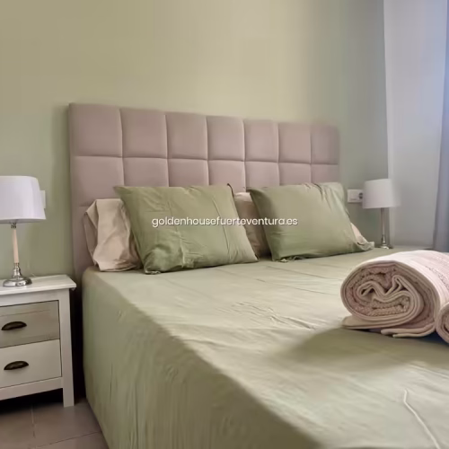 Primer plano de cama con toallas enrolladas y mesita de noche blanca con lámpara.