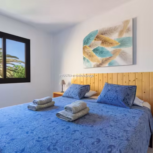 Cama preparada con juegos de toallas y cojines azules estampados en el dormitorio.